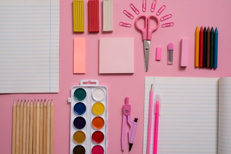 Stationary concept flat lay top view photo of scissorsschool supplies notepad and pens color pencils on a pink background pink background with copy space