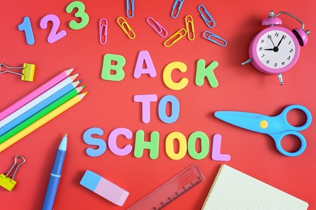 In the center of the red background the inscription is back to school made in colored letters bright colored school and office supplies are arranged around