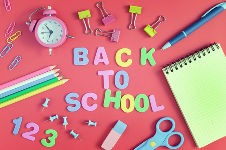 On a red background there are paperclips a notebook an alarm clock and school supplies in the center of the inscription in colored letters back to school