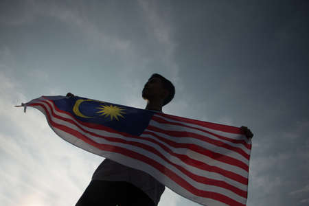 Independence day concept a happy and proud citizen holding malaysian flag sky background