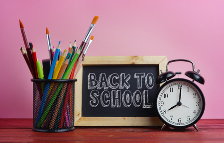 Back to school text blackboard alarm clock and school stationary in basket on wooden table pink background Stock Photo