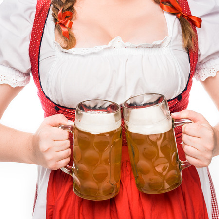 Partial view of oktoberfest waitress in traditional german dress holding mugs of light beer isolated on white background