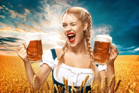 Half length portrait of young blonde with big wearing black dirndl with white blouse holding the beer mug isolated on dark background