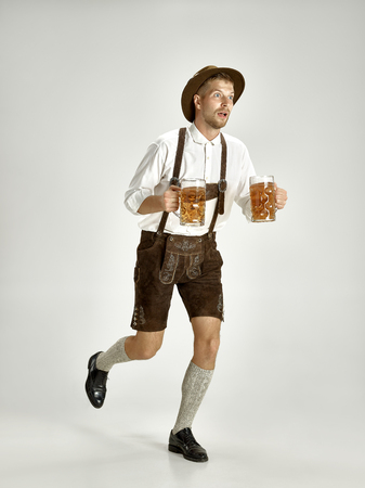 Portrait of oktoberfest young man in hat wearing a traditional bavarian clothes standing with beer at full length at studio the celebration oktoberfest festival concept