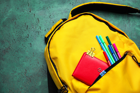 Cute rucksack with school stationery on color background