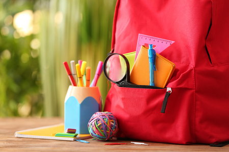 Backpack with school supplies on wooden table