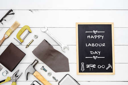 Happy labour day background concept flat lay of construction blue collar handy tools and white collar s accessories over wooden background with black chalkboard and happy labour day text