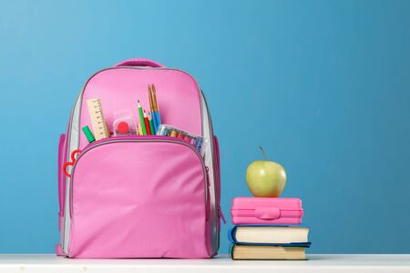 Student set pink backpack with stationery a stack of books a lunchbox an apple on the table on a blue background back to school Stock Photo