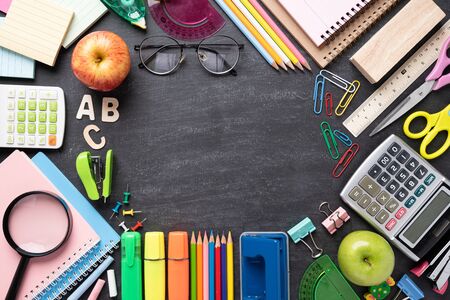 Education or back to school concept top view of colorful school supplies with books color pencils calculator pen cutter clips and green apple on chalkboard background flat lay Stock Photo