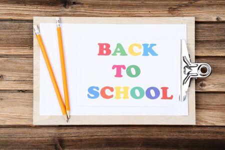 Text back to school with clipboard and pencil on brown wooden table