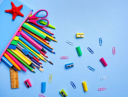 Pencil case with bright pens pencils and and other stuff on a blue background flat lay