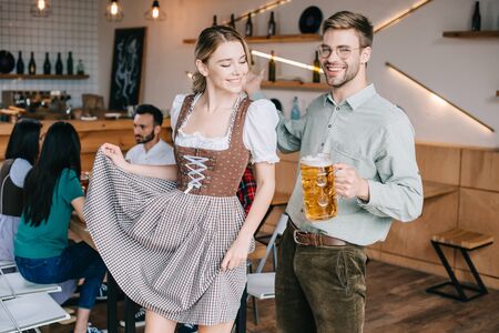 Happy man and woman in traditional german costumes holding mugs of beer