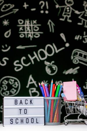 Back to school background with books pencils and globe on white table on a green blackboard background