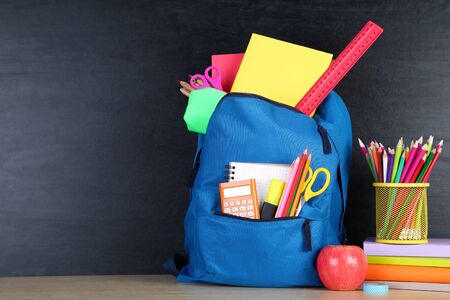 School supplies with blue backpack on blackboard background