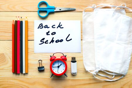 School supplies medical mask and card with message back to school on wooden background school quarantine concept