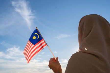 Silhouette of muslim woman in head scarf with malaysia flag at blue sunset sky concept of freedom