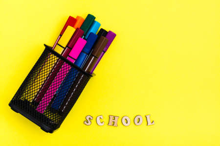 Back to school container with markers and the word school from wooden letters on a yellow background top view