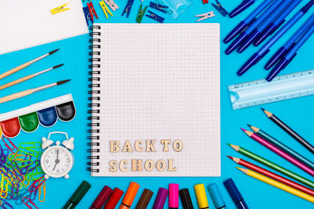 Back to school stationery alarm clock and inscription in wooden letters in a notebook on a blue background top view Stock Photo