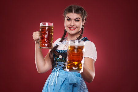 German girl in traditional costume with two large pints of pale ale over red background