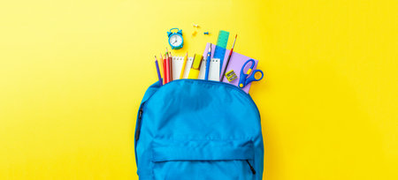 School bag backpack with supplies for school on yellow background copy space for text