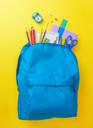 School bag backpack with supplies for school on yellow background copy space for text Stock Photo