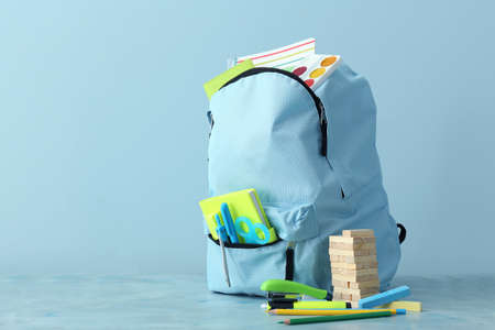 School backpack with stationery on color background