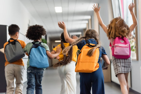 Back view of multiethnic schoolkids running in school corridor