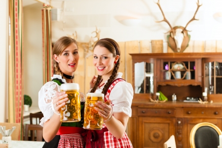 Two young women in traditional bavarian tracht in restaurant or pub with beer and beer stein