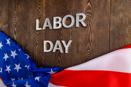 Words labor day laid with silver metal letters on wooden surface with crumpled usa flag on bottom side