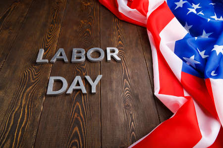 Words labor day laid with silver metal letters on wooden surface with crumpled usa flag on left side Stock Photo