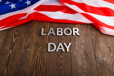 Words labor day laid with silver metal letters on wooden surface with crumpled usa flag on left side