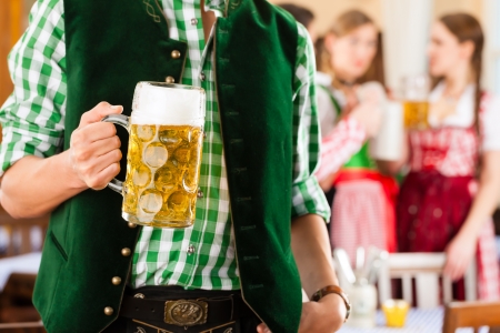 Young people in traditional bavarian tracht in restaurant or pub one man is standing with beer stein in front the group in the background