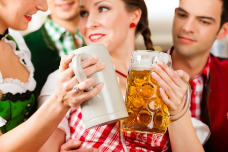 Young people in traditional bavarian tracht in restaurant or pub with beer and steins