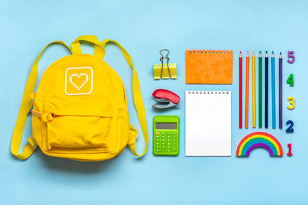 Back to school education concept yellow backpack with school supplies notebook pens eraser rainbow numbers isolated on blue background top view copy space flat lay composition