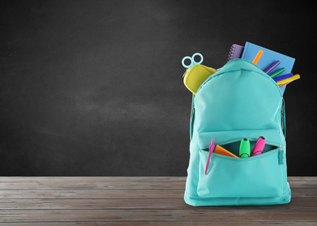 Backpack with school stationery on wooden table near black chalkboard space for text Stock Photo