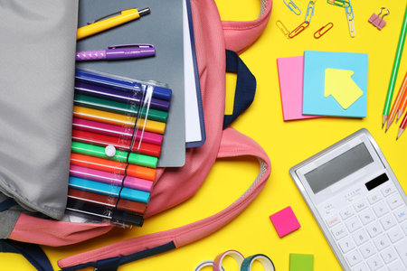 Flat lay composition with backpack and school stationery on yellow background