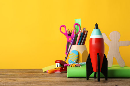 Bright toy rocket and school supplies on wooden desk space for text