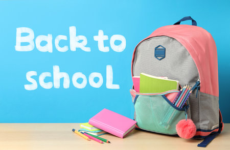 Wooden table with backpack and stationery near text back to school on blue background