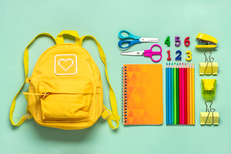 Back to school education concept yellow backpack with school supplies notebook pens eraser rainbow numbers isolated on green background top view copy space flat lay composition banner Stock Photo