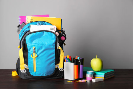 Children s backpack and different school stationery on wooden table against gray background