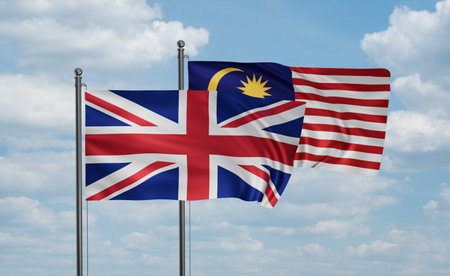 Malaysia and united kingdoms uk great britain flag waving together in the wind on blue sky two country cooperation concept