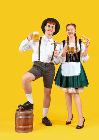 Young couple in traditional german clothes with beer and snacks on yellow background