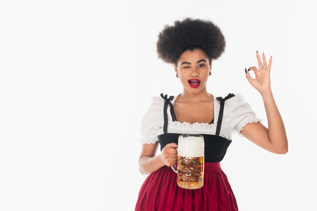 African american waitress with mug of craft beer winking and showing okay sign on white Stock Photo