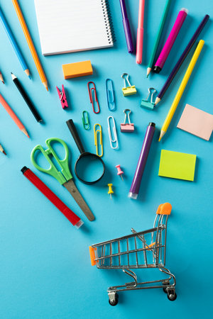 Close up of miniature shopping trolley with school materials on blue background back to school shopping school materials learning school and education concept