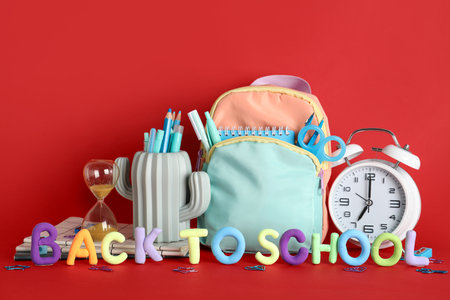 Alarm clock hourglass backpack and pencil holder with stationery behind text back to school on red background Stock Photo