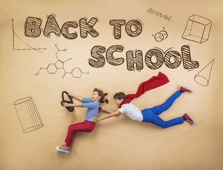 Cute boy and girl learning playfully in frot of a big blackboard studio shot on beige background