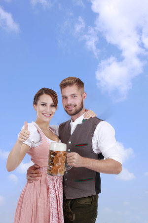 Happy young couple with beer and traditional costume in front of blue sky