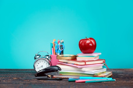 Back to school concept books colored pencils and clock on blue background