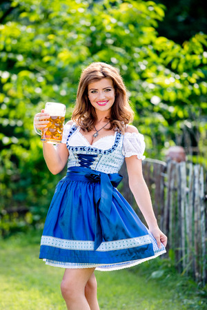 Beautiful young woman in traditional bavarian dress standing in the garden holding a mug of beer oktoberfest Stock Photo