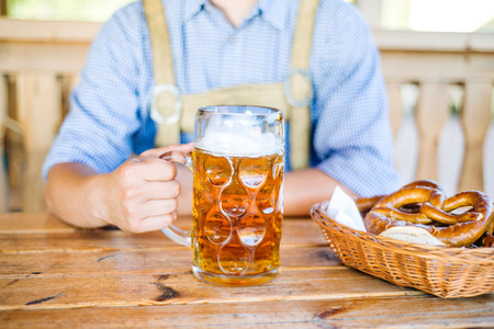 Unrecognizable man in traditional bavarian clothes sitting at the table with mug of beer pretzels in wicker basket oktoberfest Stock Photo